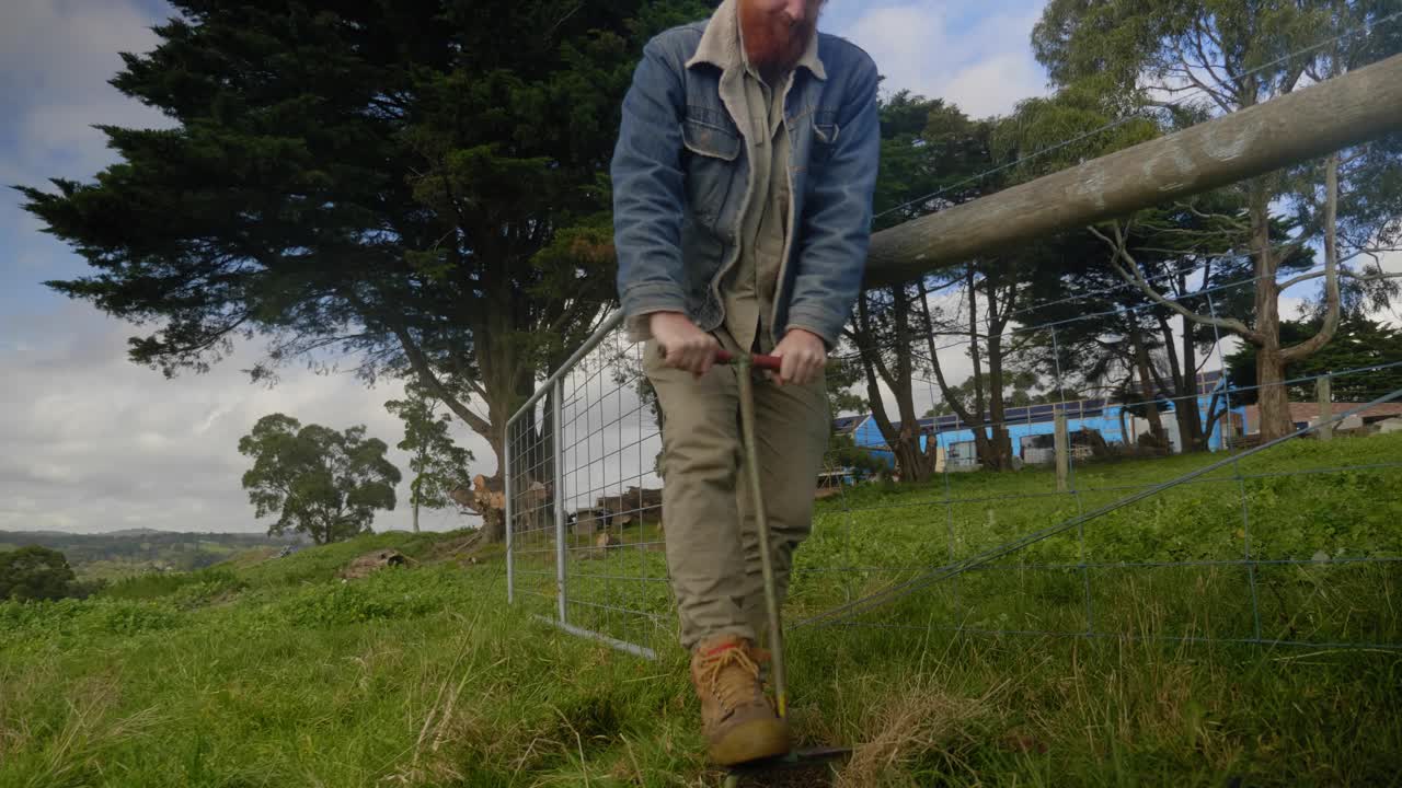 나무를 심기 위해 땅에 구멍을 뚫기 위해 정원 도구를 사용하여 농장에서 한 남자를 패닝하는 장면