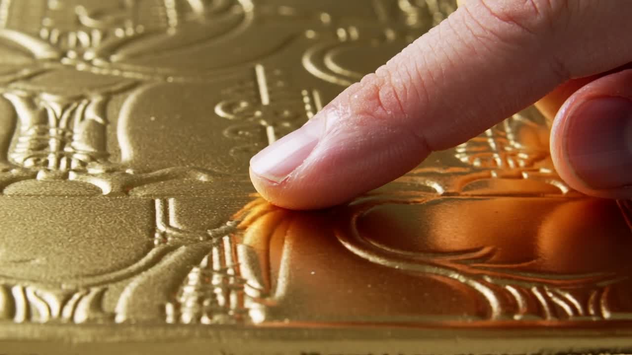 Approaching from right, index fingertip pressing, deepening dent on gold foil on table, copy space