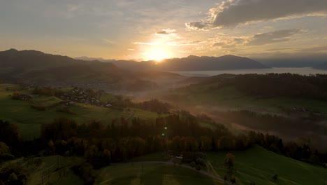 drone flight in the morning hour in autumn. the fog is down in the valley and the sun is rising behind the mountains. beautiful autumn landscape in switzerland. the clouds in the sky are illuminated.