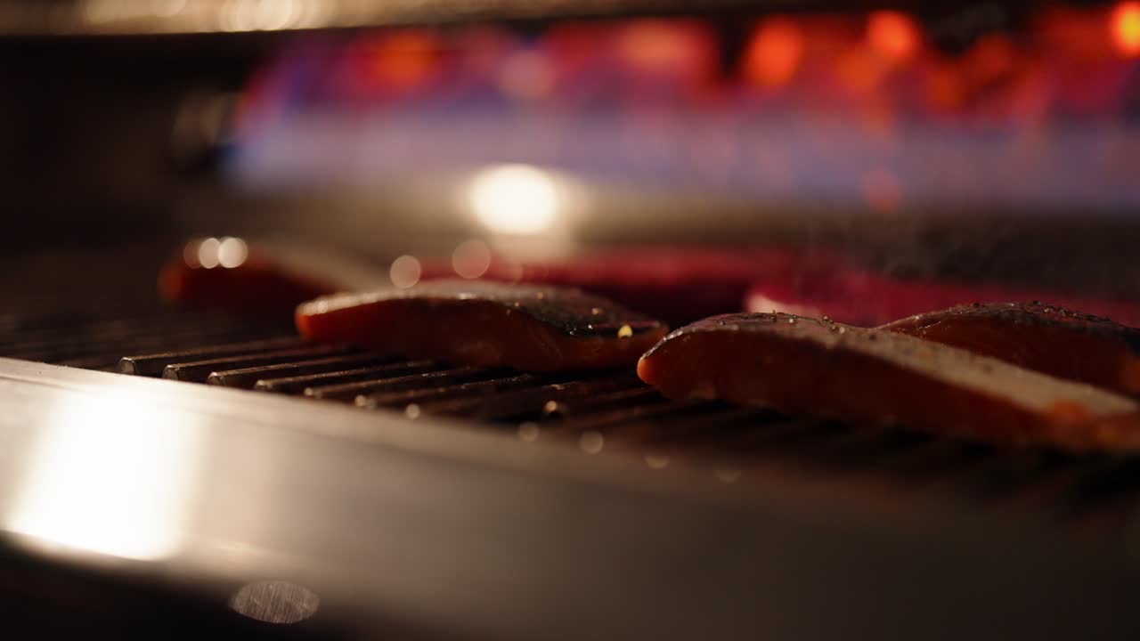 Close up clip of meat being cooked on a gas fire with a stainless steel grid and golden flames burning in the background
