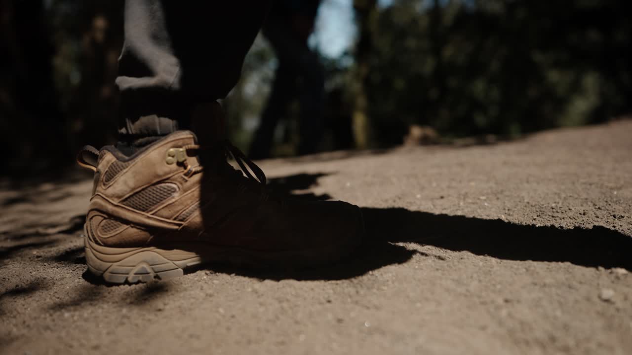 Close-up sepatu bot hiking berdebu yang menginjak pasir vulkanik di jalur Acatenango.