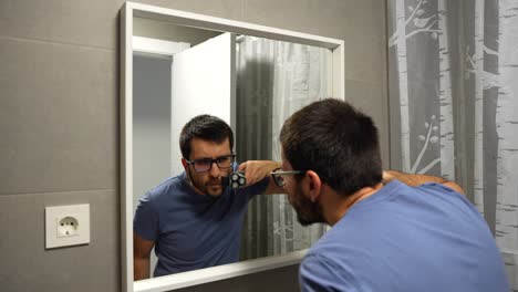 hombre afeitando el bigote con afeitadora eléctrica, reflejo en el espejo