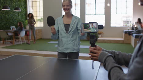 young-business-people-playing-ping-pong-in-office-enjoying-competitive-fun-colleague-using-smartphone-sharing-game-on-social-media