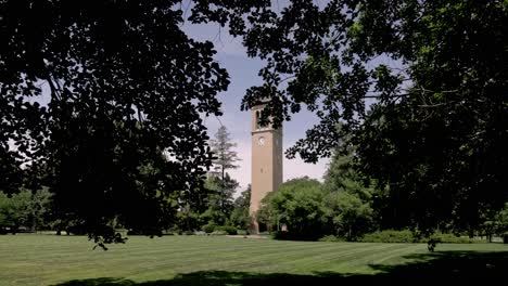 Campanile-Del-Carillón-Conmemorativo-De-Stanton-En-El-Campus-De-La-Universidad-Estatal-De-Iowa-En-Ames,-Iowa-Con-Video-De-Cardán-Caminando-Hacia-Adelante-A-Través-De-Los-árboles