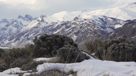 montañas patagónicas cubiertas de nieve y arbustos en invierno, cielo nublado, sereno y remoto