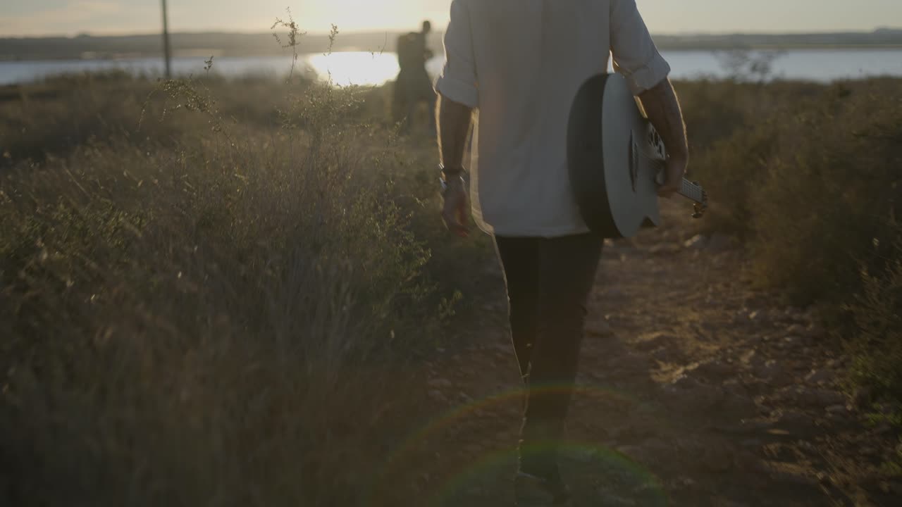 Man Walking With Guitar at Sunset