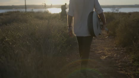 man walking with guitar at sunset