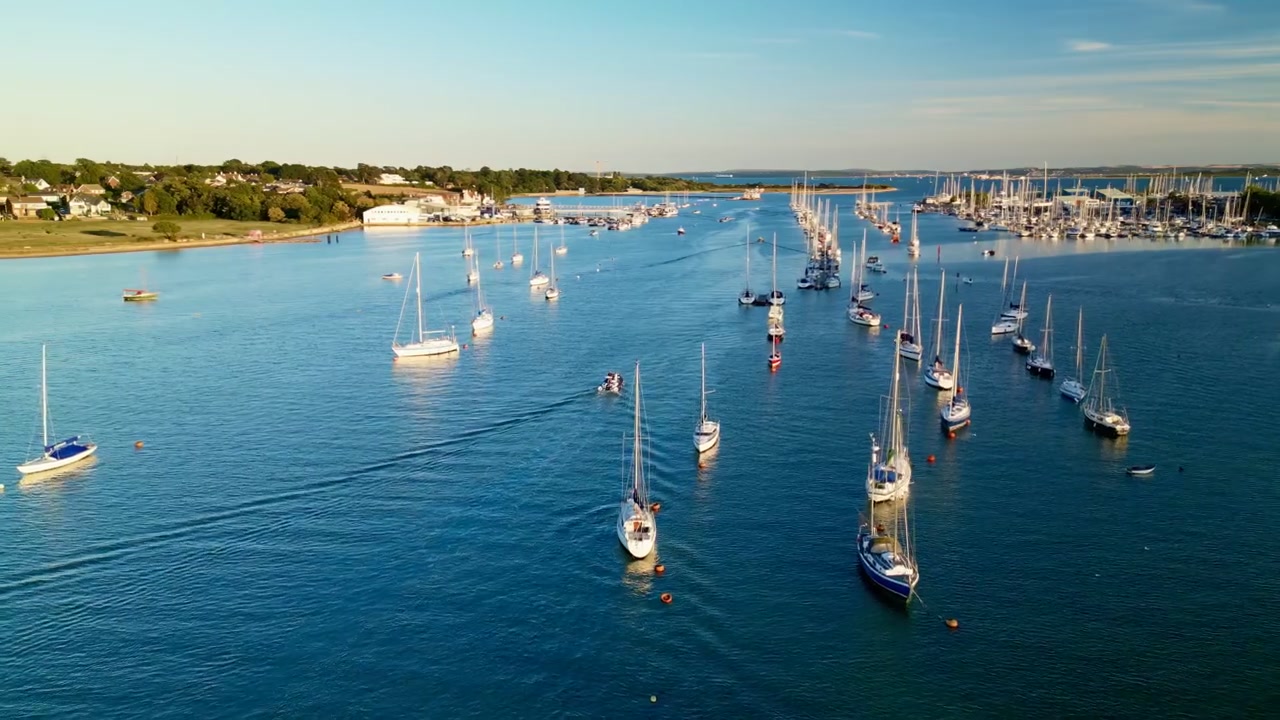 Vista aérea con dron del río Hamble, lleno de veleros y yates amarrados en aguas azules tranquilas, con costa verde e instalaciones de marina en Hampshire, Inglaterra.