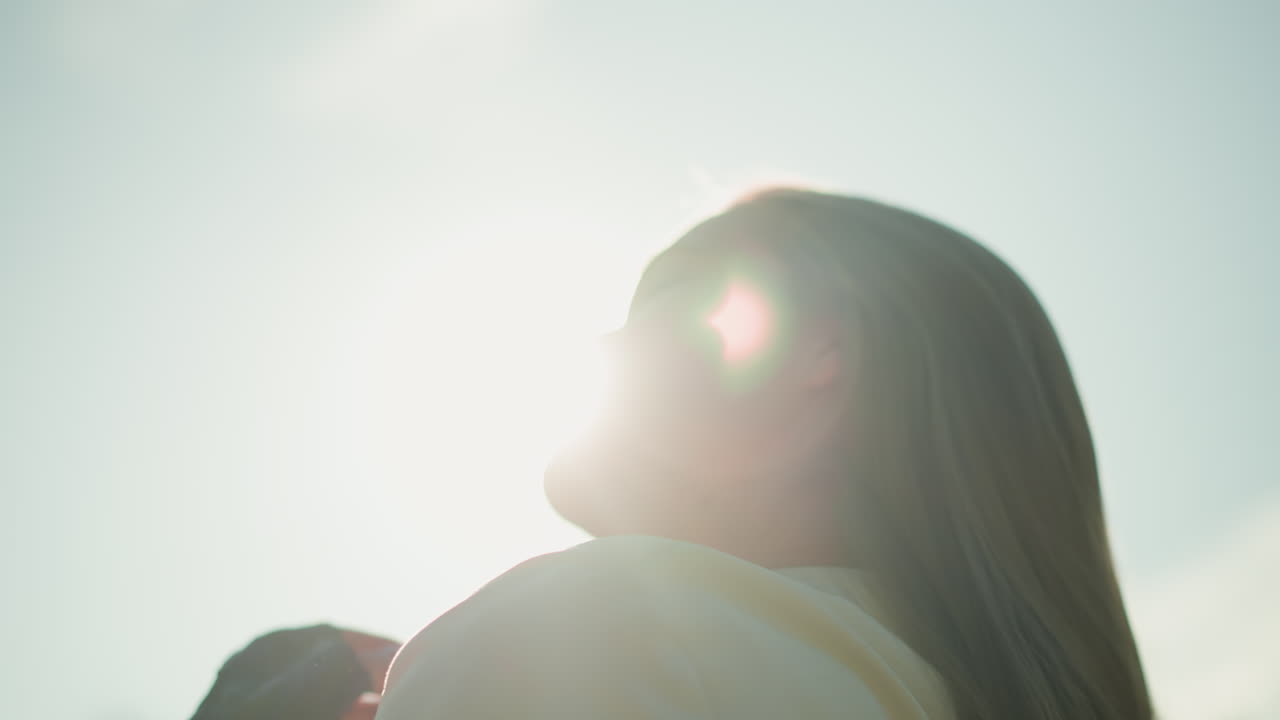 검은 장갑을 입은 여자는 머리를 뒤로 기울여, 은 빛이 그녀의 얼굴을 둘러싸고 빛나는 빛을 일으키면서 그녀의 흐르는 머리카락을 조정합니다.