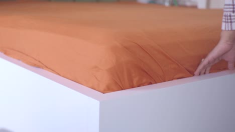 persona que hace la cama con sábanas naranjas