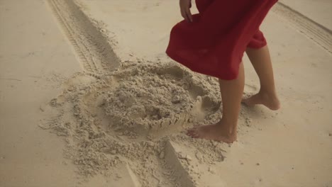 ⁇ 은 드레스를 입은 여자가 모래 위에 서서 구부러져서 모래를 손에 잡고 가지고 놀고 있습니다.