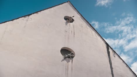 Weiße-Wand-In-Varazdin,-Mit-Zwei-Kleinen-Runden-Fenstern,-Aus-Denen-Skulpturen-Herausschauen