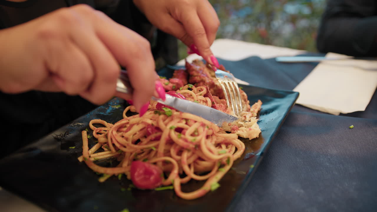 Donna che usa forchetta e coltello per mangiare aragosta nel piatto di pasta.