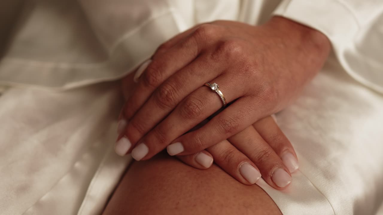 Close up of a bride's hands resting on her lap showing a delicate engagement ring