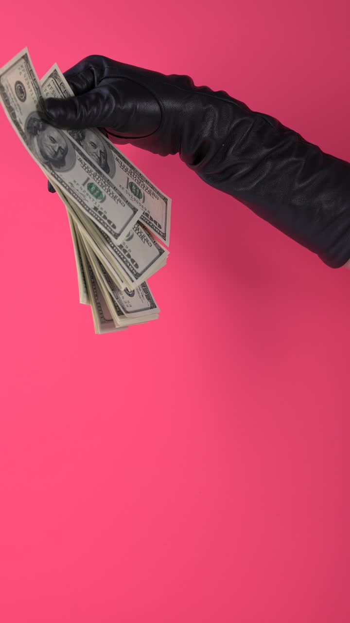 Mano guantata di nero che afferra banconote di dollari USA in caduta.