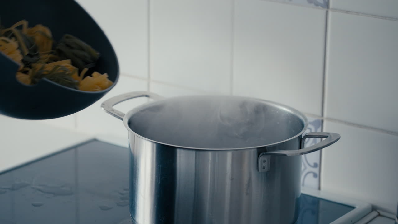 Woman's Hand opening the Lid of a big steel Pot and adding two coloured Pasta Tagliatelle to boiling Water in slow motion