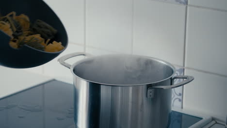 woman's hand opening the lid of a big steel pot and adding two coloured pasta tagliatelle to boiling water in slow motion