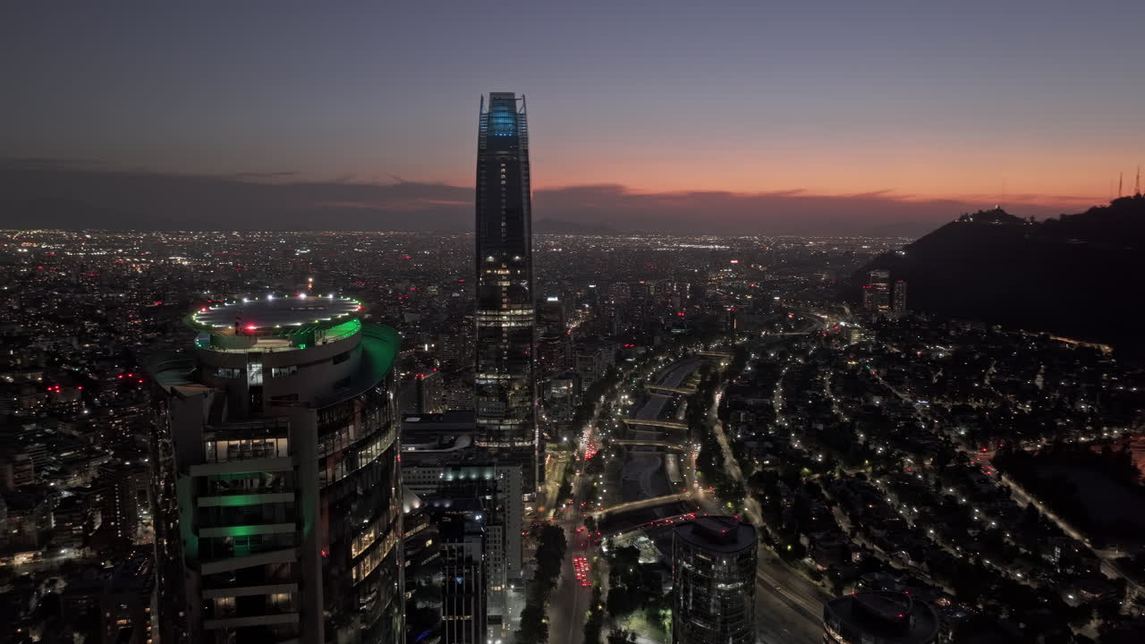 Santiago del Cile, ripresa aerea v25, sorvolo di Las Condes intorno alla Torre Titanium con viste panoramiche sul paesaggio urbano del centro, sul fiume e sul paesaggio collinare al crepuscolo - Ripresa con Mavic 3 Pro Cine - 20 gennaio 2025