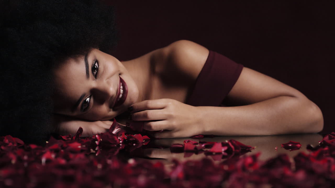 portrait d'une belle femme afro-américaine avec des pétales de rose rouge afro tombant femelle sensuelle souriante séduisante rêvant de fantaisie intime romance se livrant au désir dans le concept de la saint-valentin