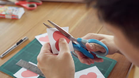 primer plano de manos cortando la forma de un corazón en papel con tijeras