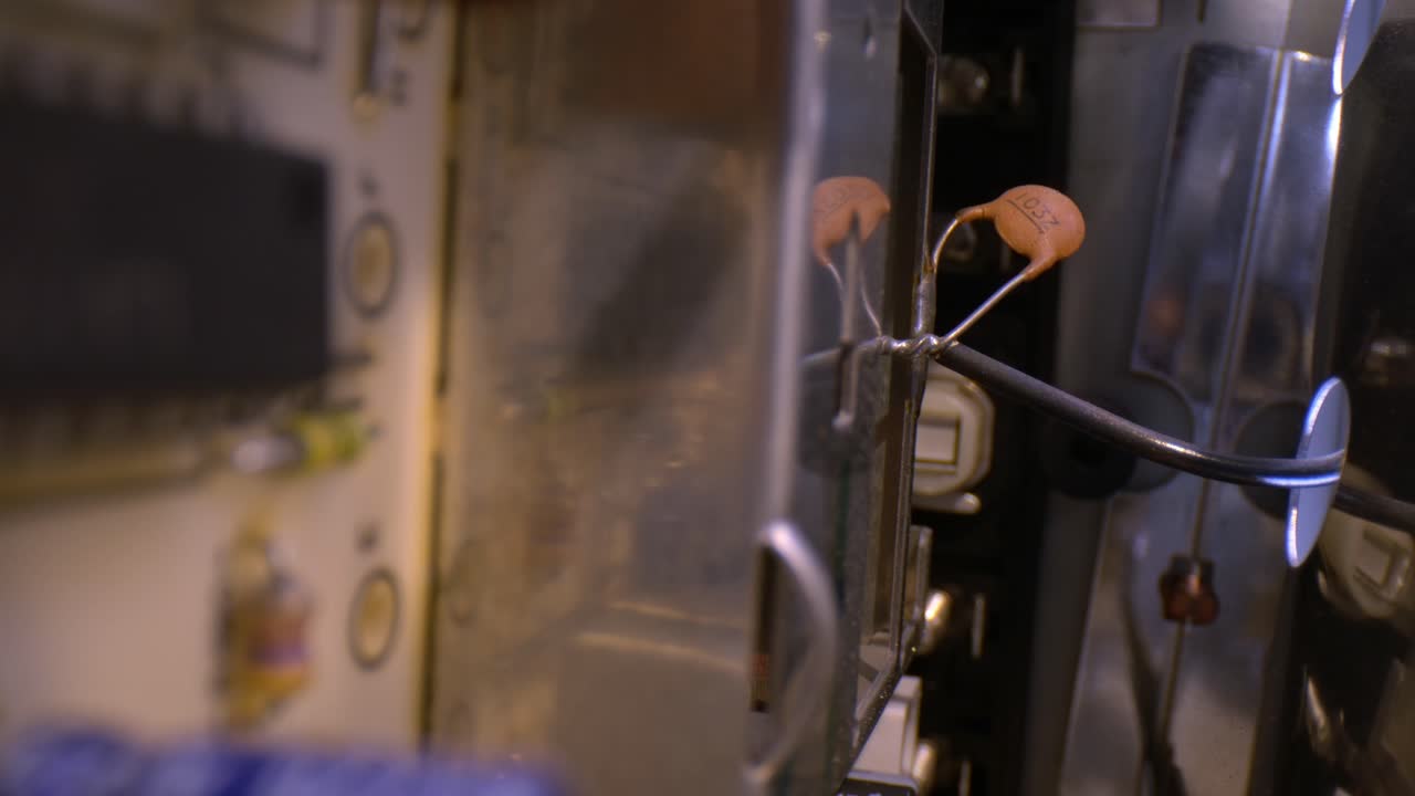 estante que enfoca un soporte y un condensador desenfocado, sacado de un amplificador estéreo antiguo con una gran cantidad de componentes electrónicos variados en una placa montada verticalmente a la izquierda