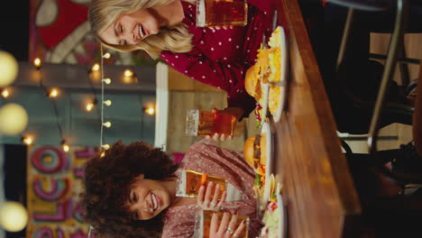 Vertical-Video-Of-Female-Friends-Sitting-At-Table-Eating-Meal-In-Restaurant-Enjoying-Girls-Night-Out