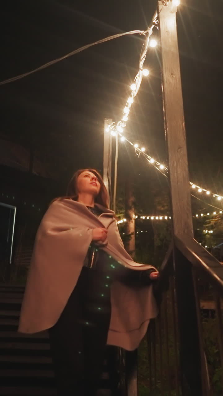 사려 깊은 여자가 뒷마당의 계단을 내려가며, 사려깊은 여자는 늦은 저녁에 집의 잘 조명된 사적인 공간을 산책합니다.