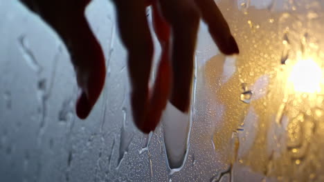 hand touching wet window with rain drops