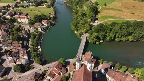 drone pushes over aarburg’s red‑roof castle and church with bridge over aare river flowing through historic swiss old town in canton aargau
