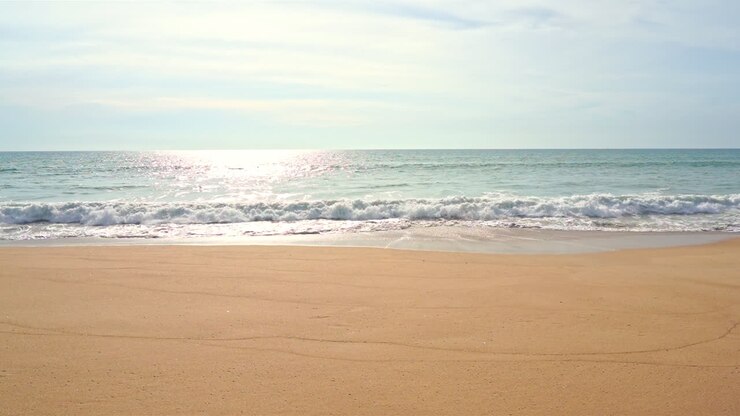 Waves crashing on beach and sunlight reflections on sea surface