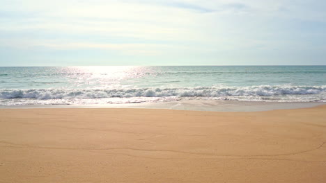 Waves-crashing-on-beach-and-sunlight-reflections-on-sea-surface