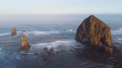 beautiful sunrise on the oregon coast - mossy haystack rock and crystal clear blue water crashing against the pacific ocean coast, sea birds flying above 4k 30fps aerial drone footage high static shot