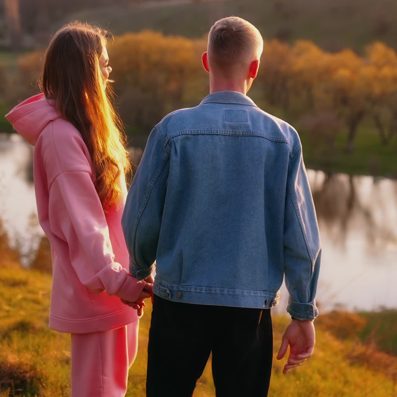 Romantic couple at sunset. Beautiful girl and her boyfriend standing in nature and looking at the setting sun. Happy young people talk near the river