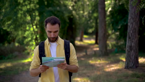 hiker man with backpack walks along a forest trail looking at a map. medium shot, front view.