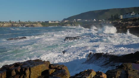 Toma-Panorámica-De-Las-Olas-Rompiendo-Violentamente-En-La-Costa-Rocosa-De-Hermanus,-Sudáfrica