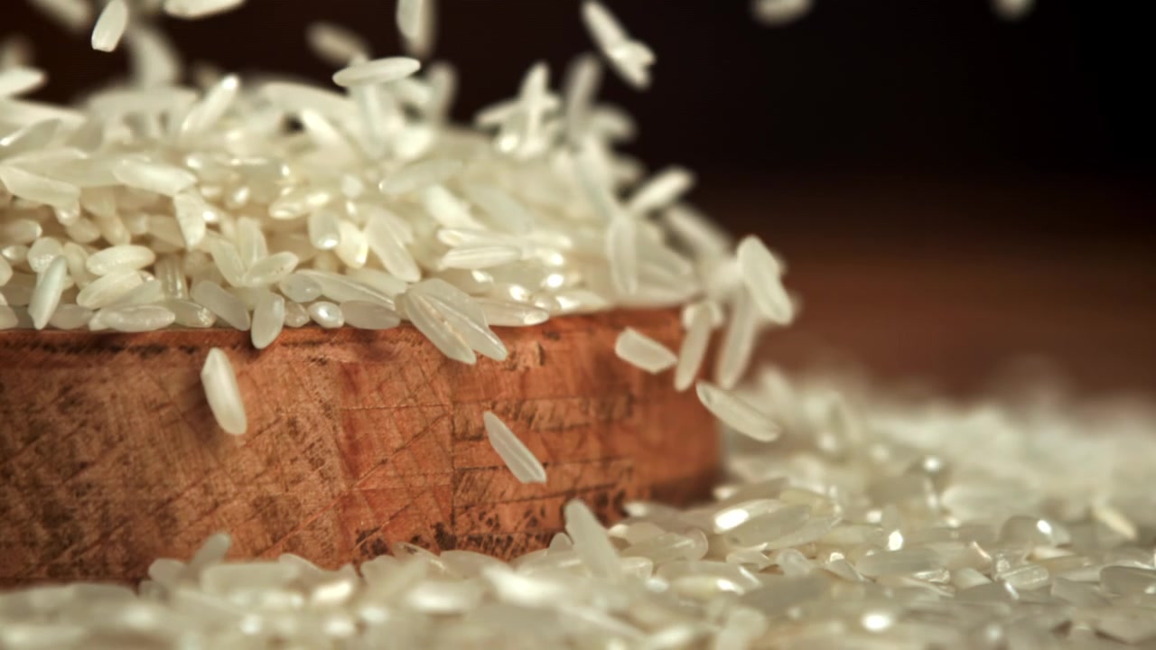 Granos de arroz blanco cayendo en un cuenco de madera en cámara lenta