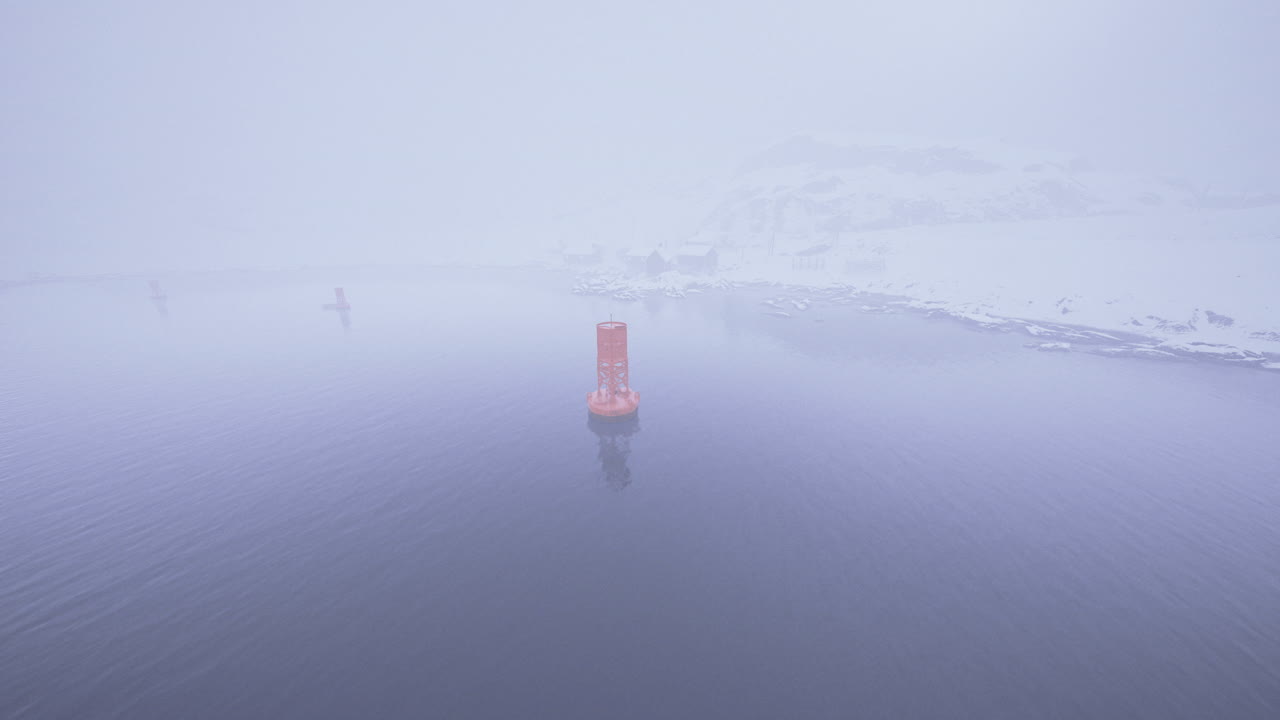 Bright orange buoy stands out in foggy waters near snowy shore