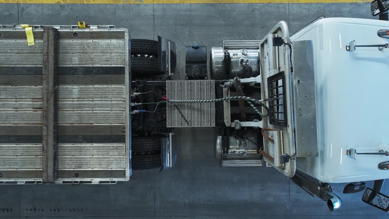 el dron desciende de arriba hacia abajo hasta el punto de conexión del tractor de camión a la cama plana en el almacén