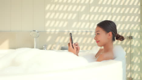 An-attractive-young-woman-in-a-luxurious-bubble-bath-checks-her-smartphone-and-social-media