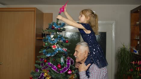 niña y abuelo anciano decorando el pino artificial de navidad en la casa de la habitación a la vieja moda