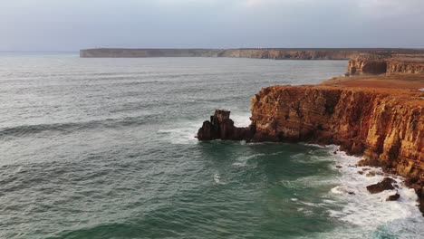 Eroded-sea-cliffs-of-Tonel-beach-in-south-Portugal-splashed-by-large-waves,-Aerial-flyover-reveal-shot