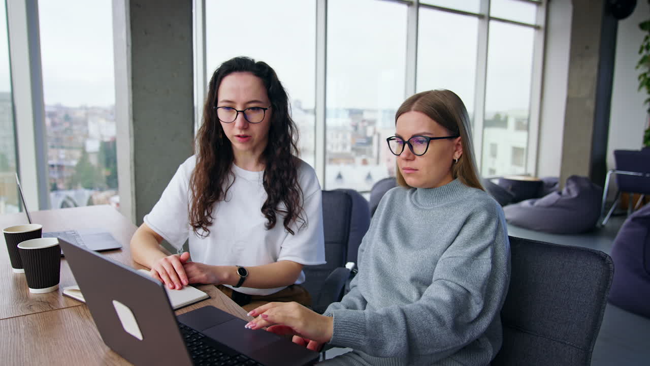 Female colleagues sit in the office working on laptop. Workmates discussing the project.