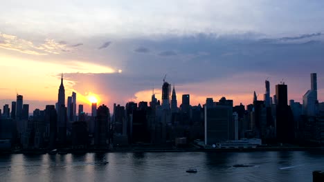 an aerial drone, time lapse clip moving towards the city view with a beautiful sunset as the backdrop behind the new york city skyline, as boats in the river below moving on about their business