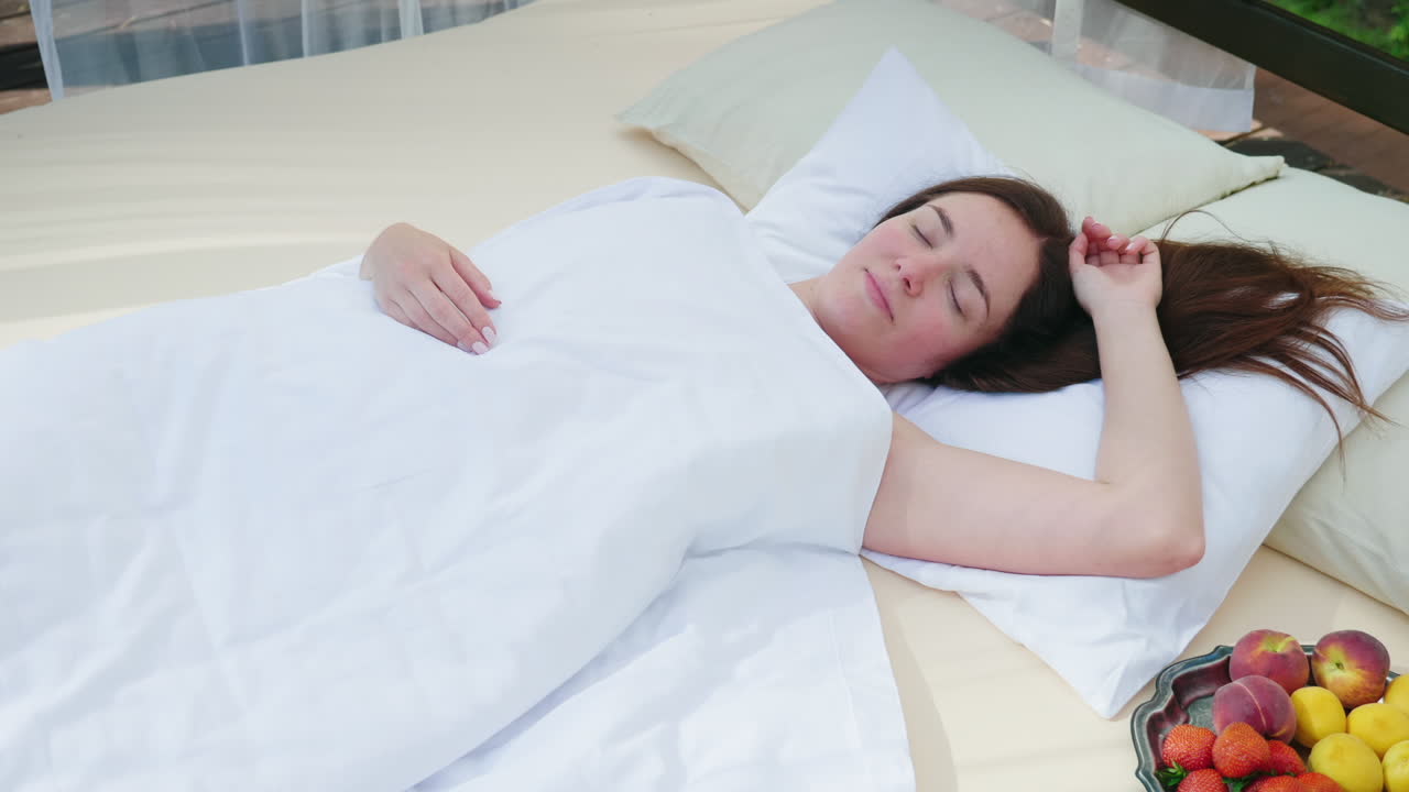 한 젊은 여성이 그녀 근처에 커튼으로 덮인 안락 의자에서 깨어납니다. 과일 화려한 로망티 한 접시