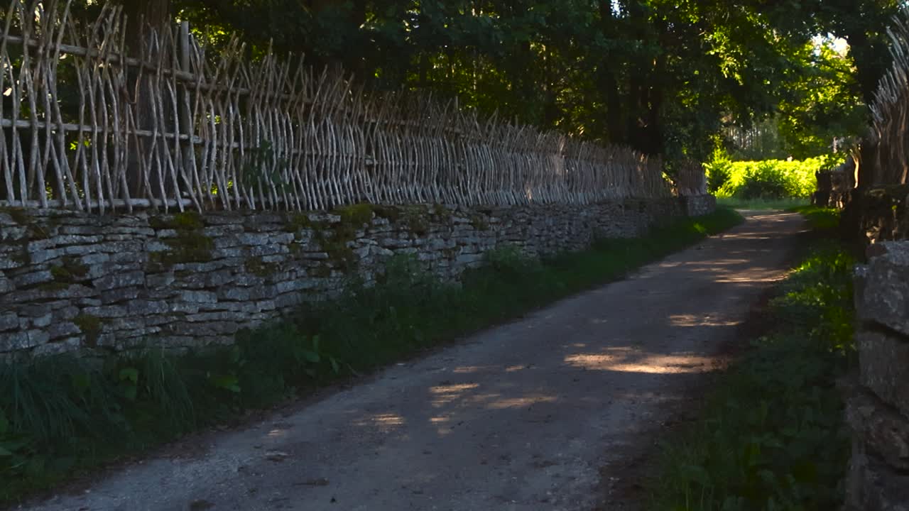 Lonely and empty pathway or road in between traditional limestone rock walls or fences that have moss covering them and also stick wooden fence on them during a summer sunny day. Traditional structure