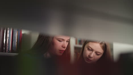 women read book together in library closeup. young students choose educative literature in shop view through bookshelf. interested readers