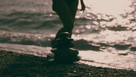 woman in bikini walking among the waves against the background of stones balancing on the beach.