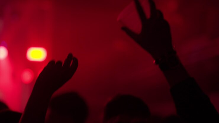 Sagome di persone che alzano le mani e i bicchieri a un concerto illuminato di rosso