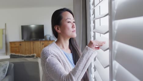 profile of thoughtful asian woman standing at window, looking outside