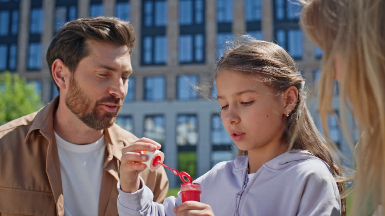 Playful family blowing soap bubbles on weekend picnic meadow together closeup